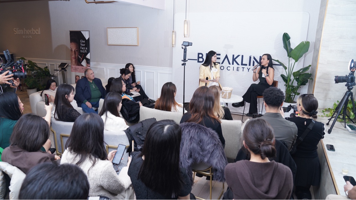Lucia Liu in a yellow blazer in conversation with a guest speaker on stage at the Women in AI and FinTech gathering, seen over the audience
