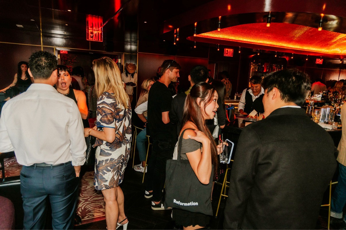 Guests mingling around the bar under warm red-gold light at the NYC Tech Week Rooftop Mixer