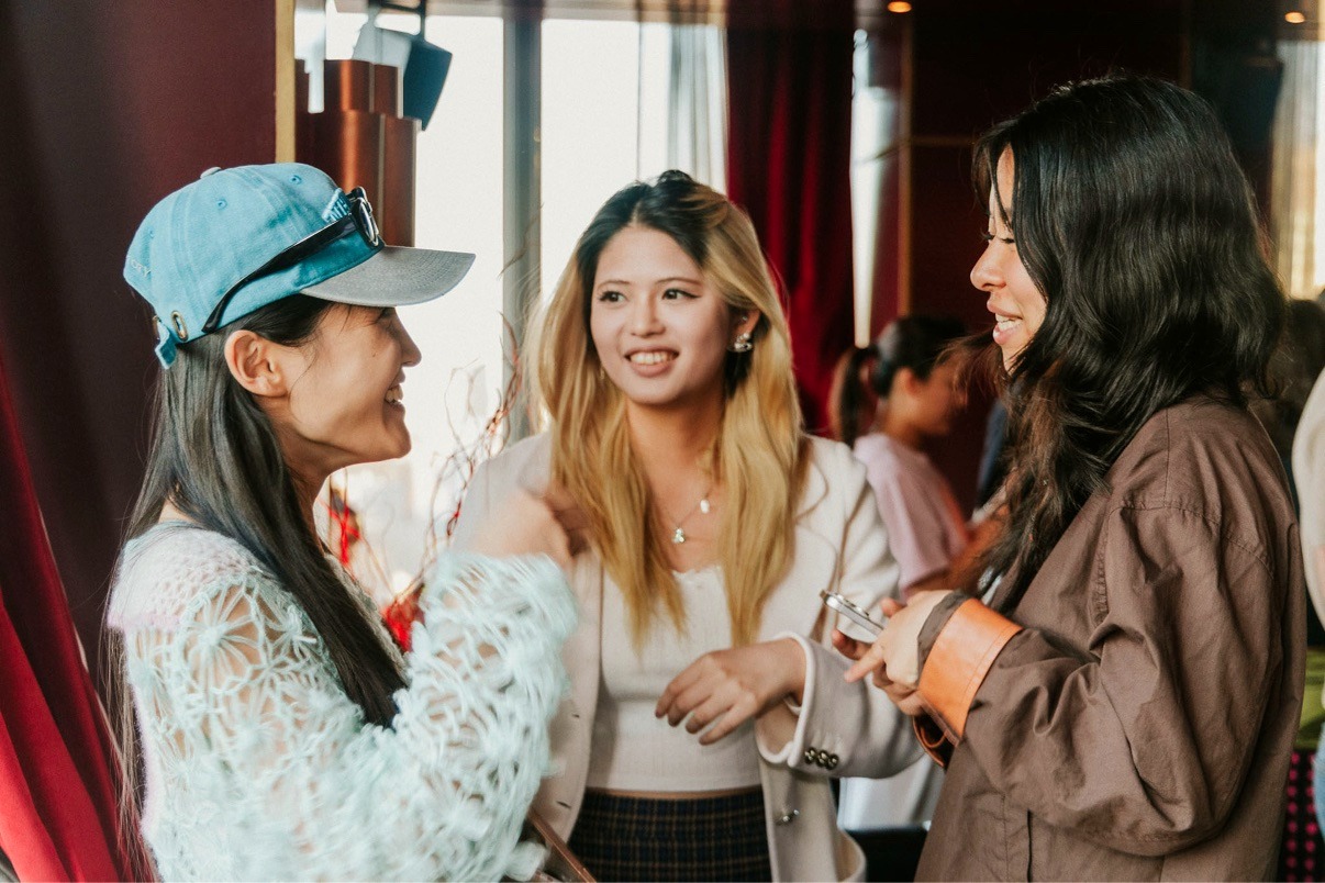 Three guests talking and smiling in warm evening light at the NYC Tech Week Rooftop Mixer